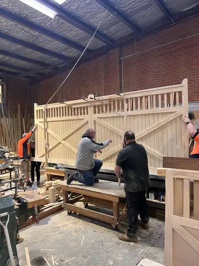 Workshop staff assembling and checking a large pair of decorative timber driveway gates.