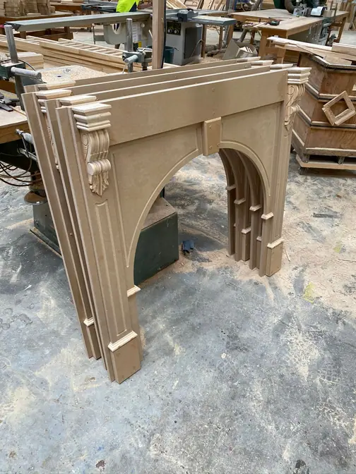 A large moulded timber arch surround standing on the workshop floor with further arched sets stacked behind it.