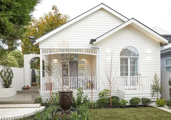 White weatherboard cottage with arched fretwork along its verandah