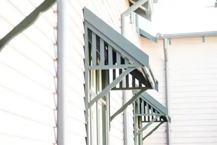 Green slatted timber window canopies on a pale weatherboard wall