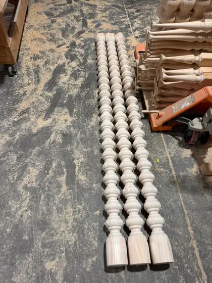 Bobbin-turned timber lengths on the workshop floor beside a pallet of turned spindles