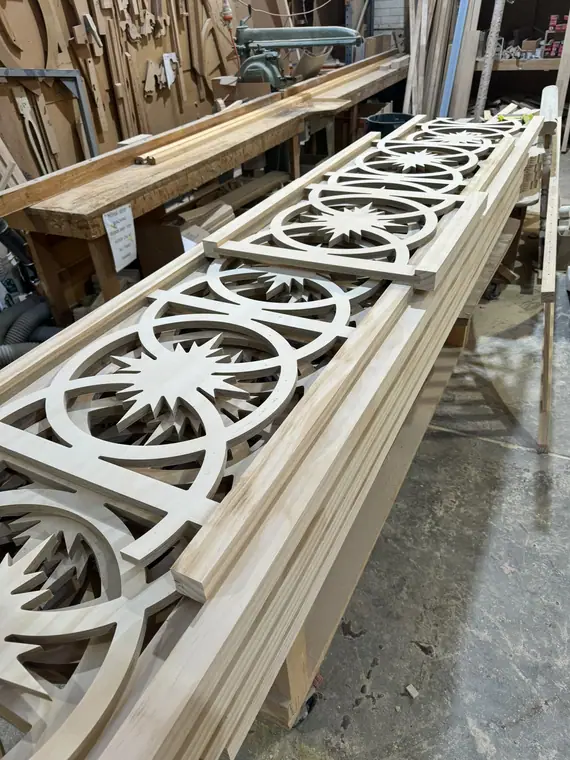 Long pierced timber fretwork panels laid out on a workshop bench