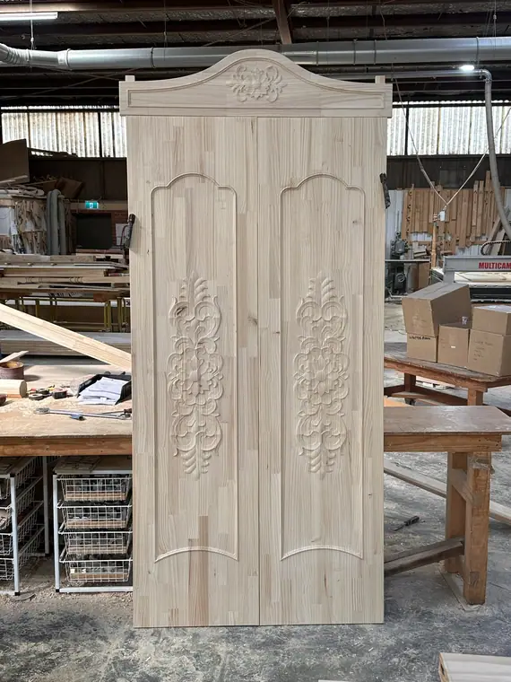 A pair of carved arched-panel timber doors, shown before finishing.