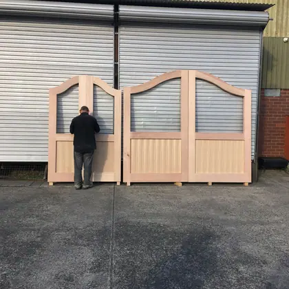 Three arched-top hardwood gate leaves standing outside the Heritage factory, one being worked on