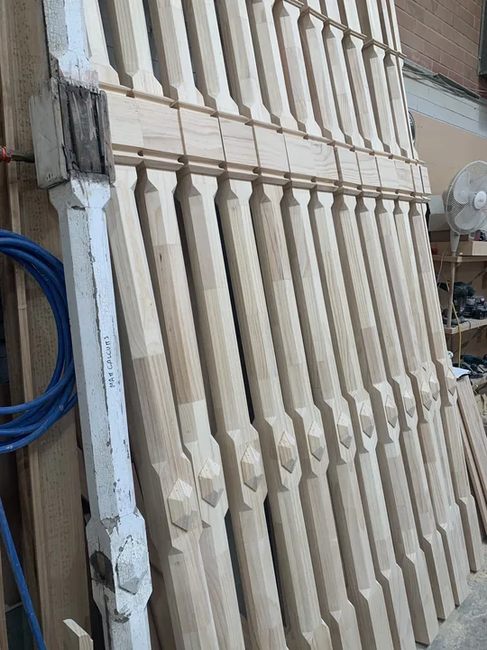 Weathered painted decorative post beside a batch of new matching timber posts