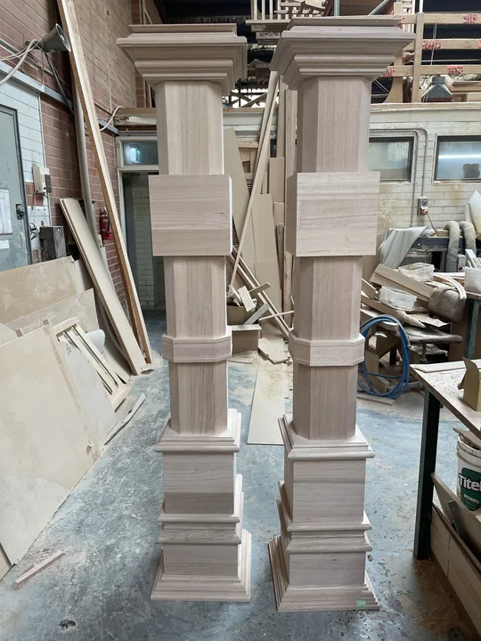 Two newly made decorative timber columns with shaped capitals and bases in the workshop