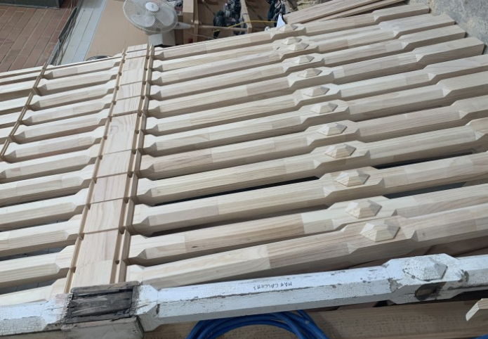 Machined timber balusters stacked beside the machine that shaped them
