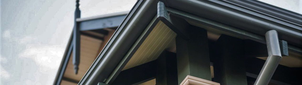 Wide banner crop of a dark metal roof edge and eaves above a timber stair landing