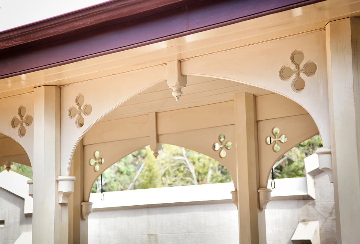 Arched fretwork brackets seen from beneath a verandah, the garden showing through the quatrefoil pierces