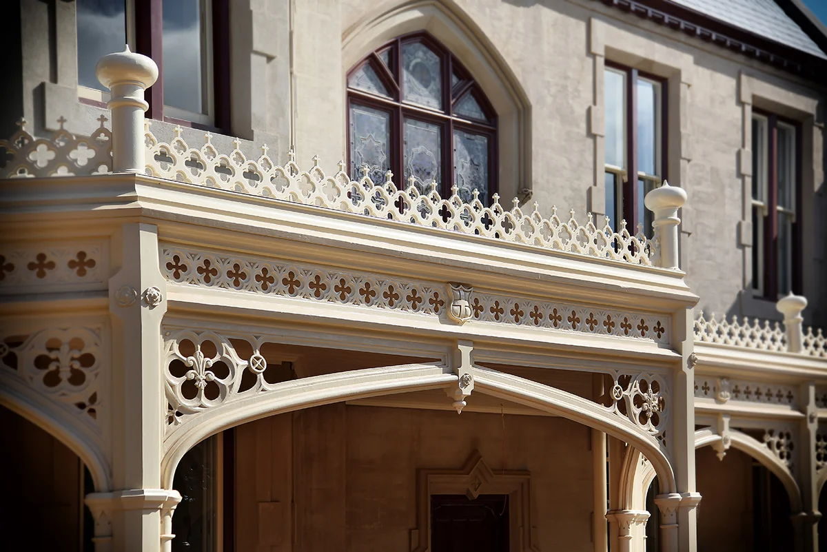 Arched verandah fretwork against a stone facade, below a leadlight Gothic window