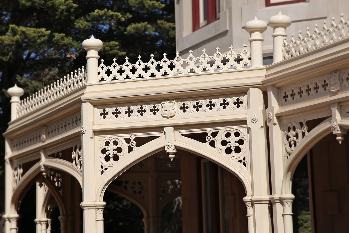 The corner of a verandah where two runs of arched fretwork meet, under quatrefoil cresting and onion finials