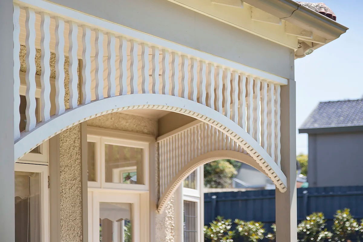 An arched fretwork valance with a dentil-moulded edge, over the bay window of a roughcast bungalow