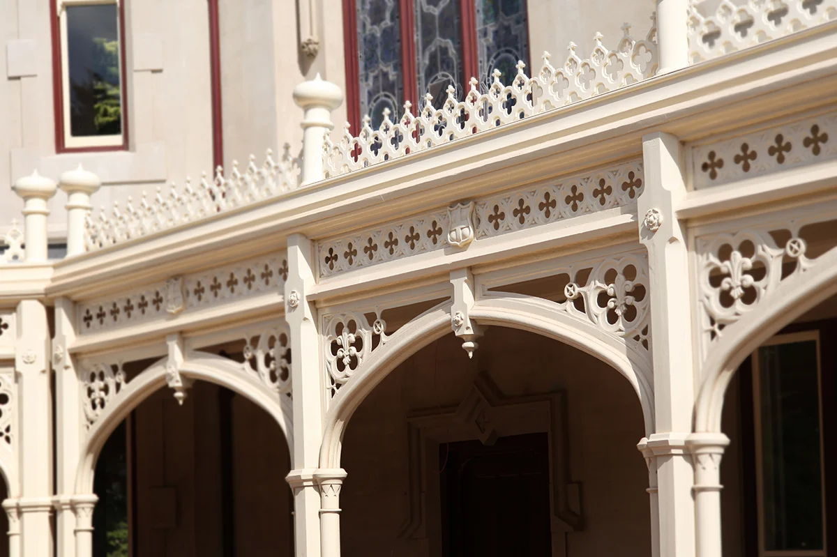 Arched verandah fretwork on a rendered stone house, with a quatrefoil frieze and cresting above