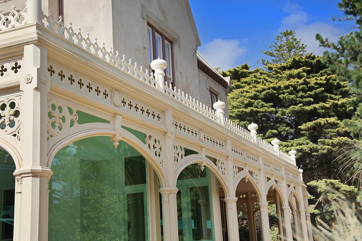A long verandah colonnade of arched fretwork, the glazing behind it reflecting the garden