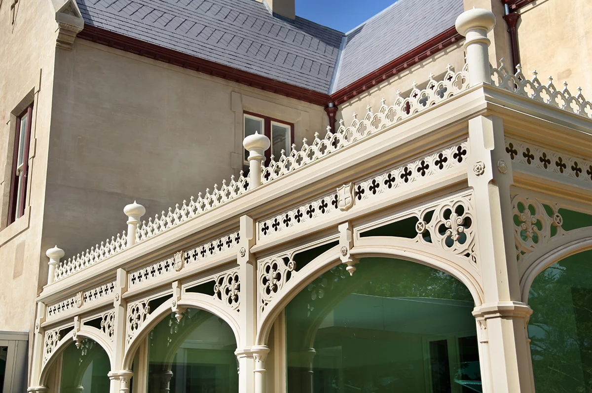 Arched fretwork at the corner of a verandah, below a slate roof and quatrefoil cresting